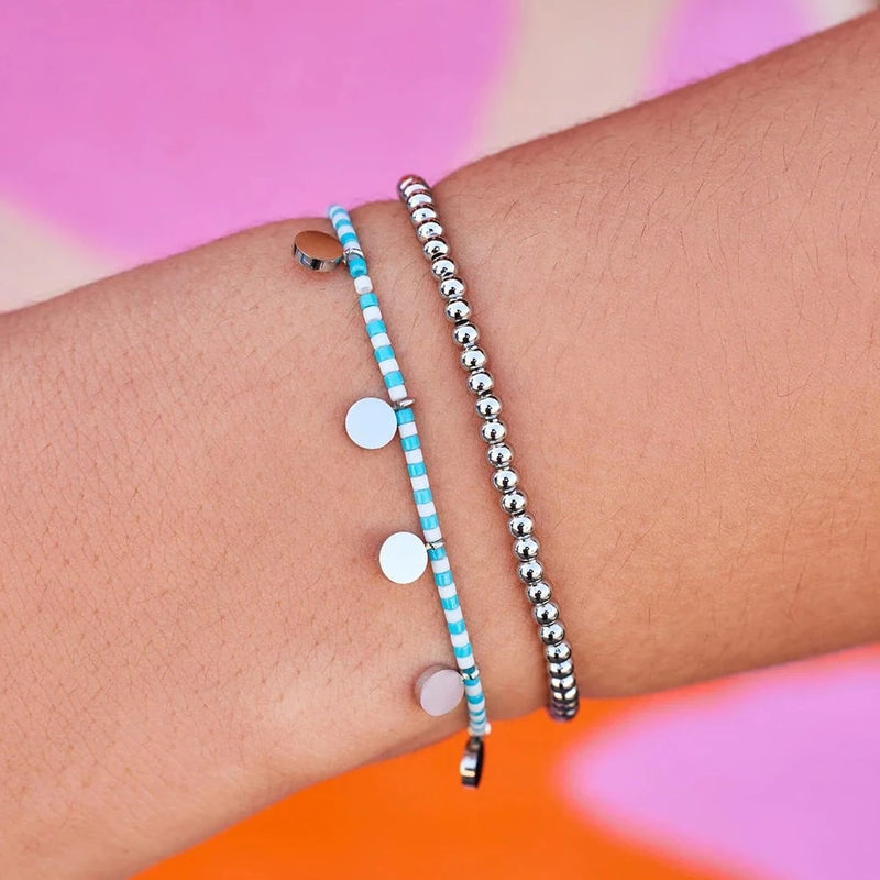 Model is wearing both bracelets from the silver set. One bracelet is made up of solid silver beads and the other is blue and white beads with flat silver circular charms hanging off.