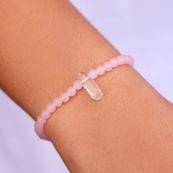 Shows stretch bracelet on models wrist. Features pink rose quartz beads with a clear raw quartz stone in center.