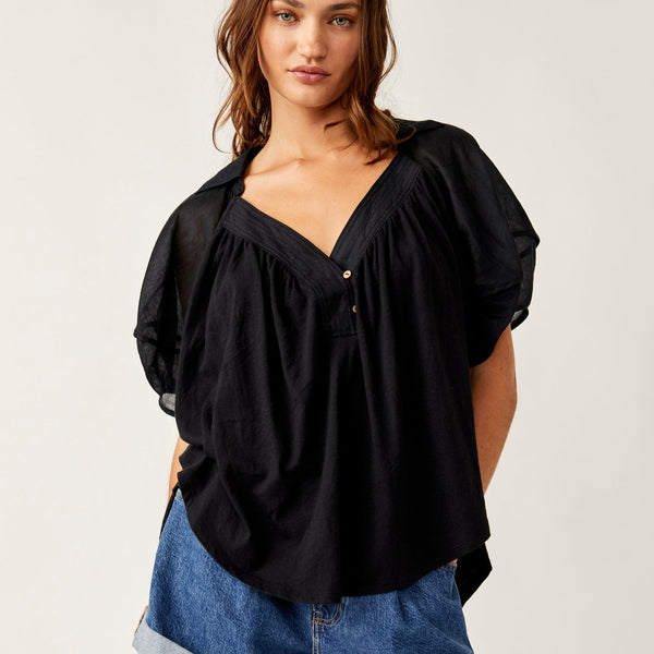 front view of the model wearing the sunray babydoll top. shows the collared neckline. also shows the puffy sleeves, the asymmetrical hem line and exposed seam details.   