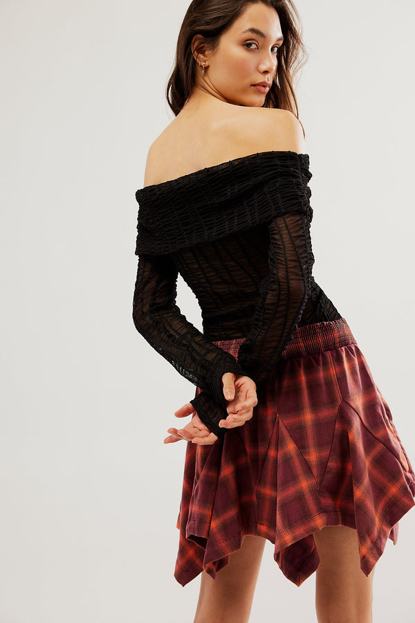 back/side view of model wearing XIA plaid mini skirt in burgundy. shows the asymmetrical pleating. also shows the mid rise fit. 