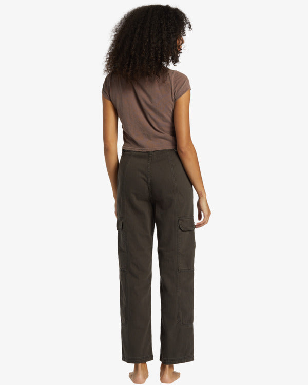 Back view of model wearing cargos. Shows the two side flap pockets on each side. Also shows the high waisted fit, the back has no back pockets, the straight leg that hits right around the ankle and the color of the cargos are black sands. 