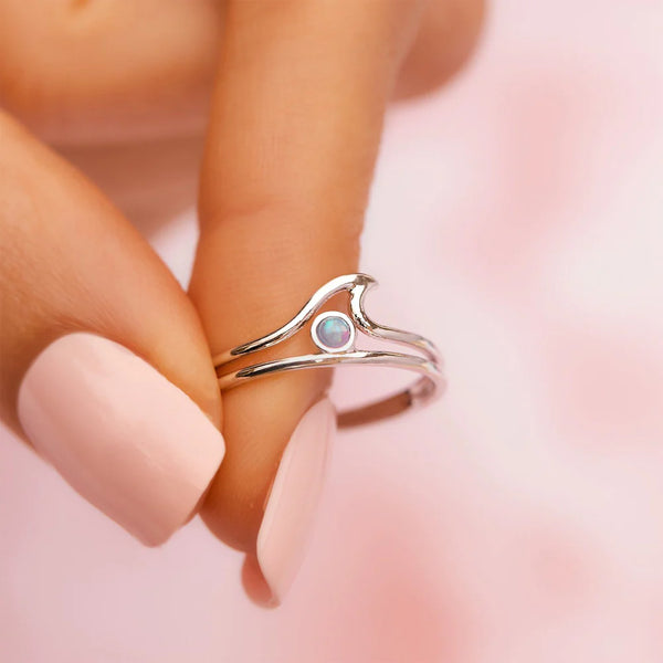 shows model holding a silver ring with cut out wave detail and an opal stone in the center.