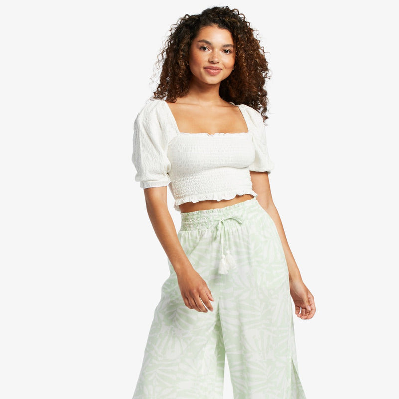 front view of model in the white crop top. shows the smocked bodice, square neckline, puff sleeves and ruffled hemline.