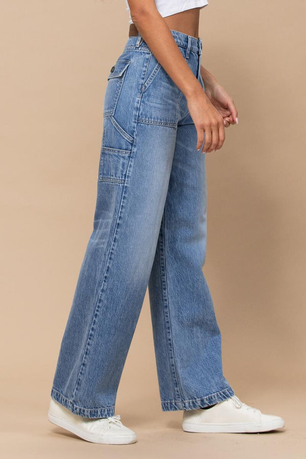 angled side view of model in jeans. here you can see the side pockets, a back pocket with a flap is visible at this angle. you can also see some faded whispering and the wider legs.