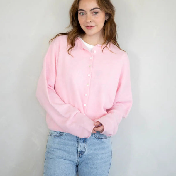 Person wearing a pink hoodie and blue jeans against a plain background