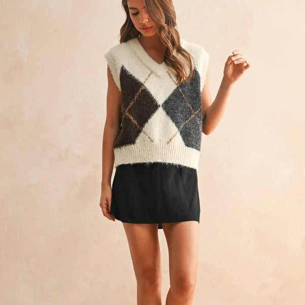 Woman wearing a sleeveless, patterned sweater with a plain background