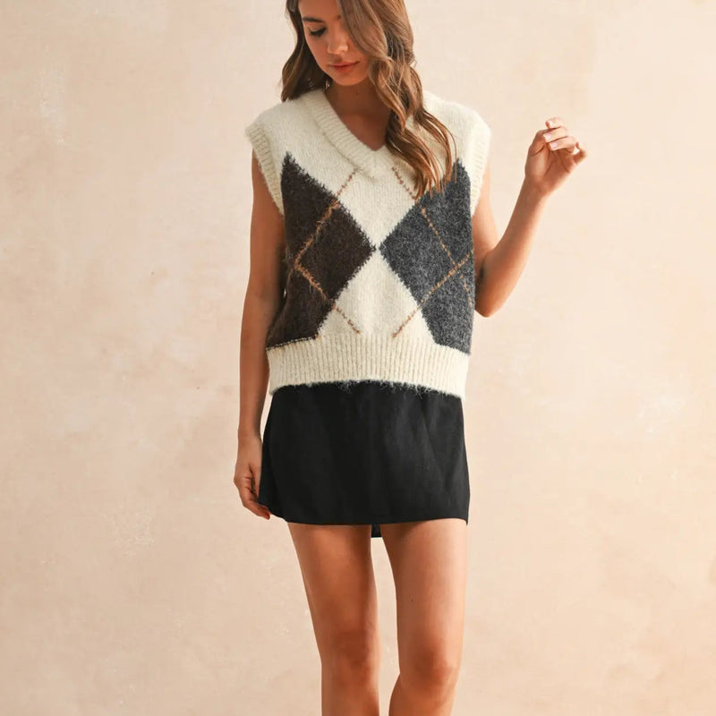 Woman wearing a sleeveless, patterned sweater with a plain background