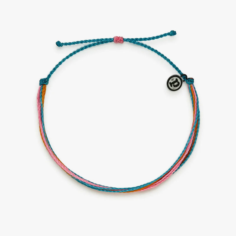 shows a white backdrop under anklet made of teal, pink, and orange wax coated strings. features a metal disc charm with a "p" inside