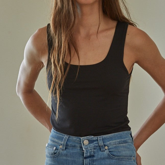 front view of model wearing the black tank top. shows the tank top tucked in, the fitted silhouette, scoop neckline and thick straps.