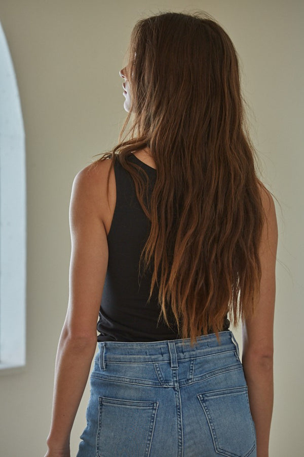 shows back view of model in the black tank top. shows the tank top tucked in, the fitted silhouette and the fully covered back.