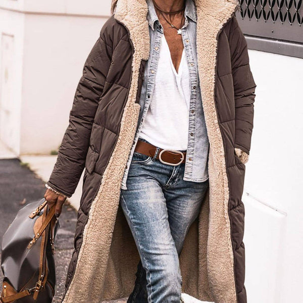Person wearing a long brown coat with a fur-lined hood, blue jeans, and brown boots on a street.