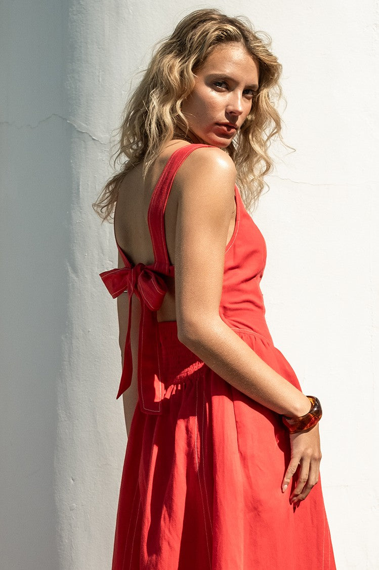 side/back view of the amelia dress. shows the smocked backing. also shows the tie bow detail on the back, the wider strap and the red color. 