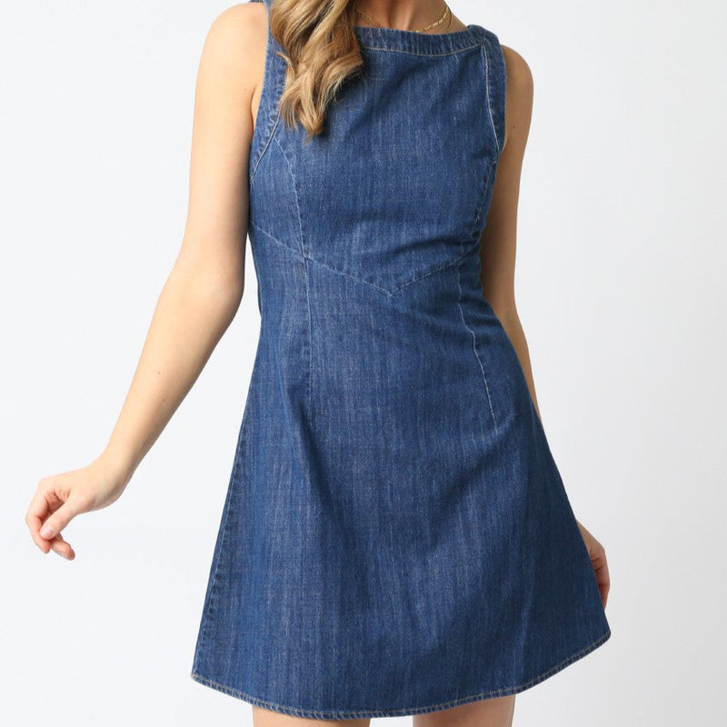 front view of the model wearing the maya denim dress. shows the boat neckline. also shows the a line style, the denim look, and that the dress is sleeveless. 