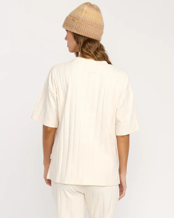 Person wearing a beige beanie and white outfit on a plain background