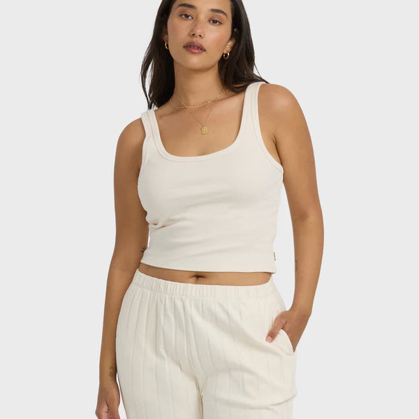 Woman wearing a white tank top and pants on a plain background