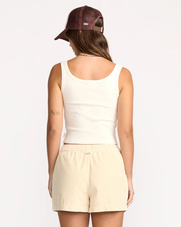 Person wearing a beige tank top and shorts with a brown cap on a white background
