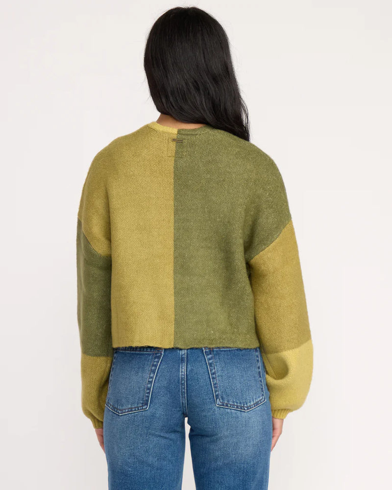 Person wearing a green and yellow sweater with blue jeans on a white background