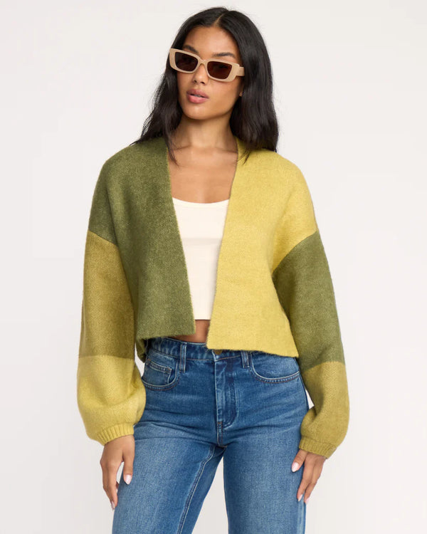 Woman wearing a two-tone green and yellow sweater with blue jeans on a white background