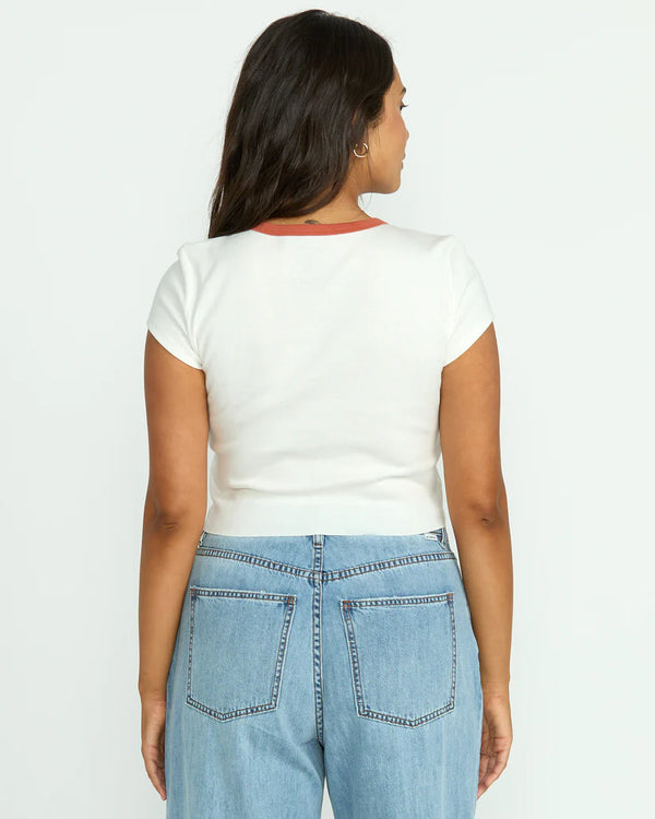 back view of the model wearing the electric feeling top. shows the solid white back. also shows the cropped/snug fit, the red trim on the neckline. 