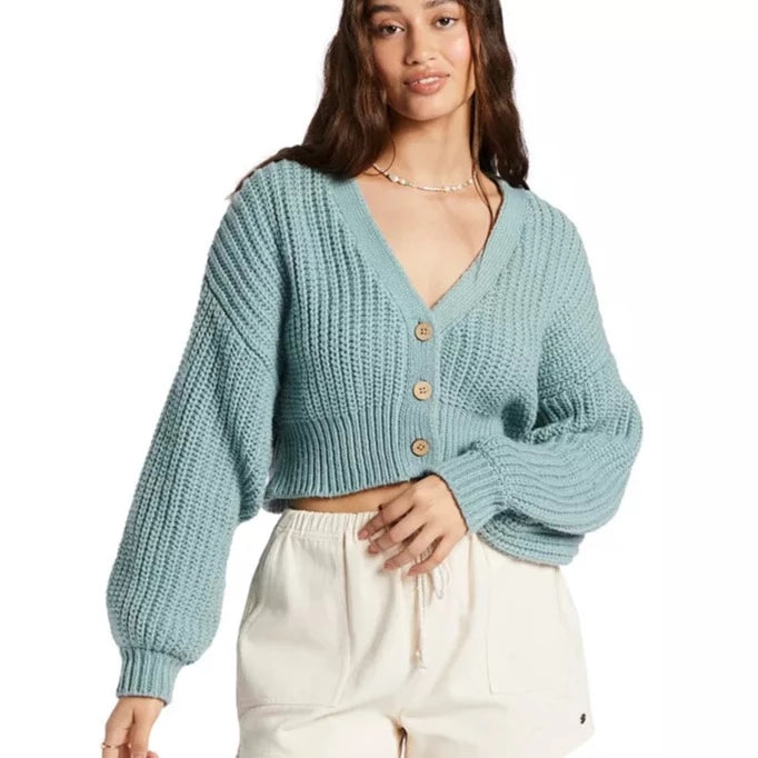 front view of model in blue cardigan. shows the cropped length, v-neckline, dropped shoulders and blouson long sleeves. shows a boxier fit. 3 coconut buttons run down the front.