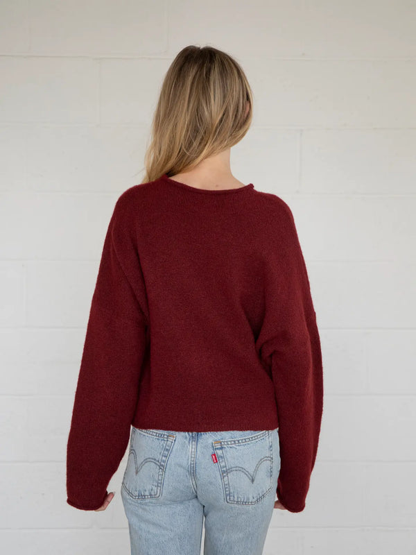 back view of the model wearing the wine cardigan wearing blue jeans against a white background. 