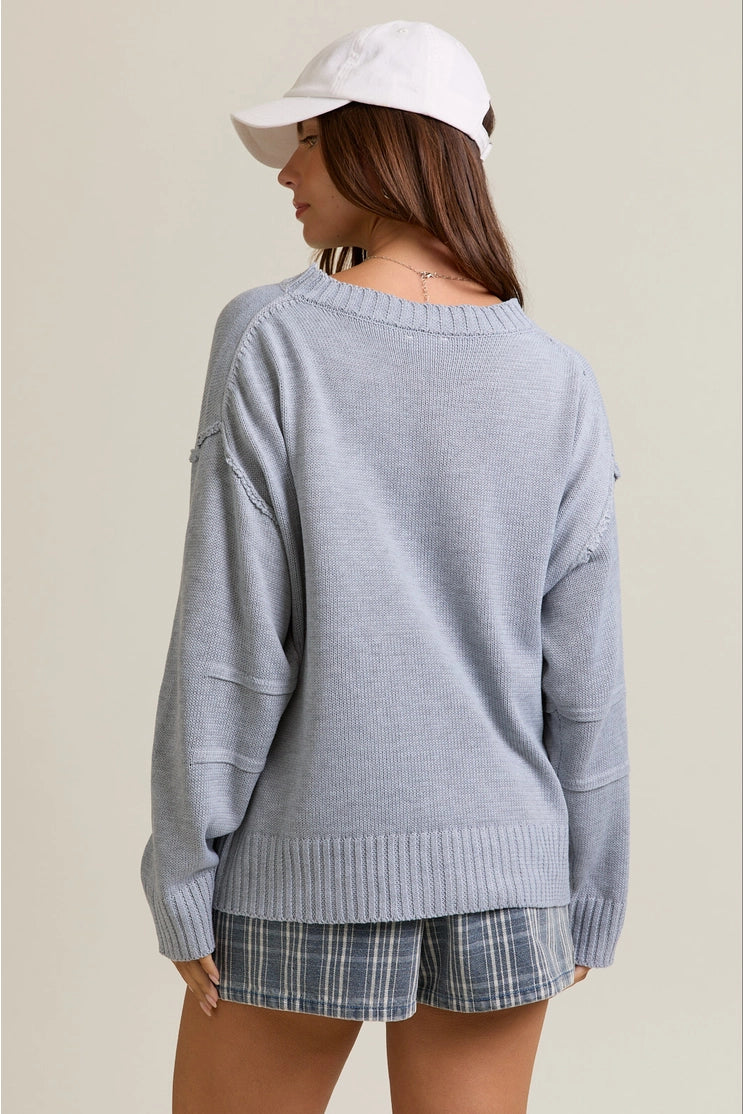 back view of the model wearing the rosy sweater top. shows the longer back. also shows the ribbed detailing, the drop shoulders, the heather grey color, and the pleated sleeves. 