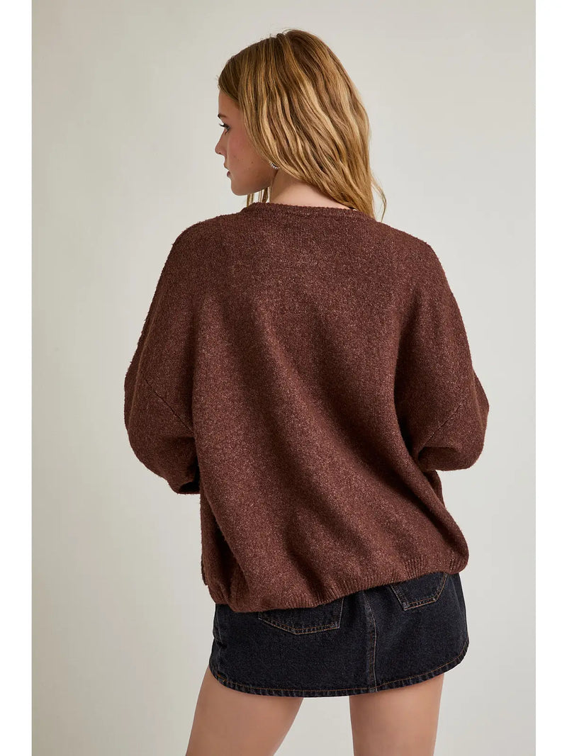 model wearing the brown cardigan, wearing a black skirt on the cream background. 