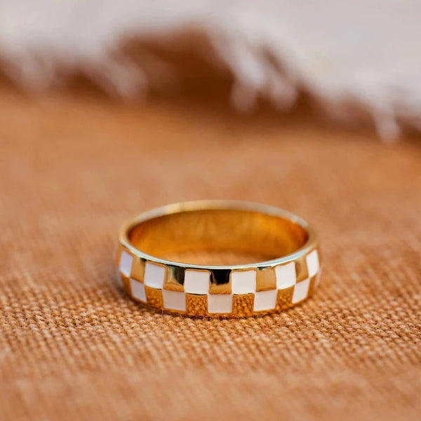Shows gold ring on a flat surface. Shows white and gold checkered design.