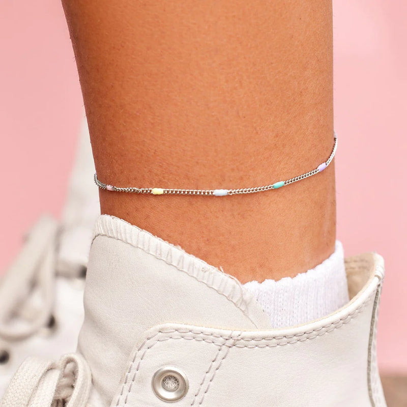 shows an ankle with a silver chain anklet lined with pink, yellow, light blue, teal, and purple enamel beads