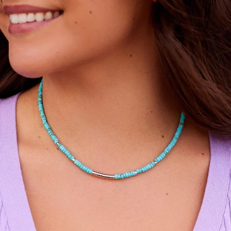 Model is wearing choker which has small blue flat beads with some silver flat beads added throughout.