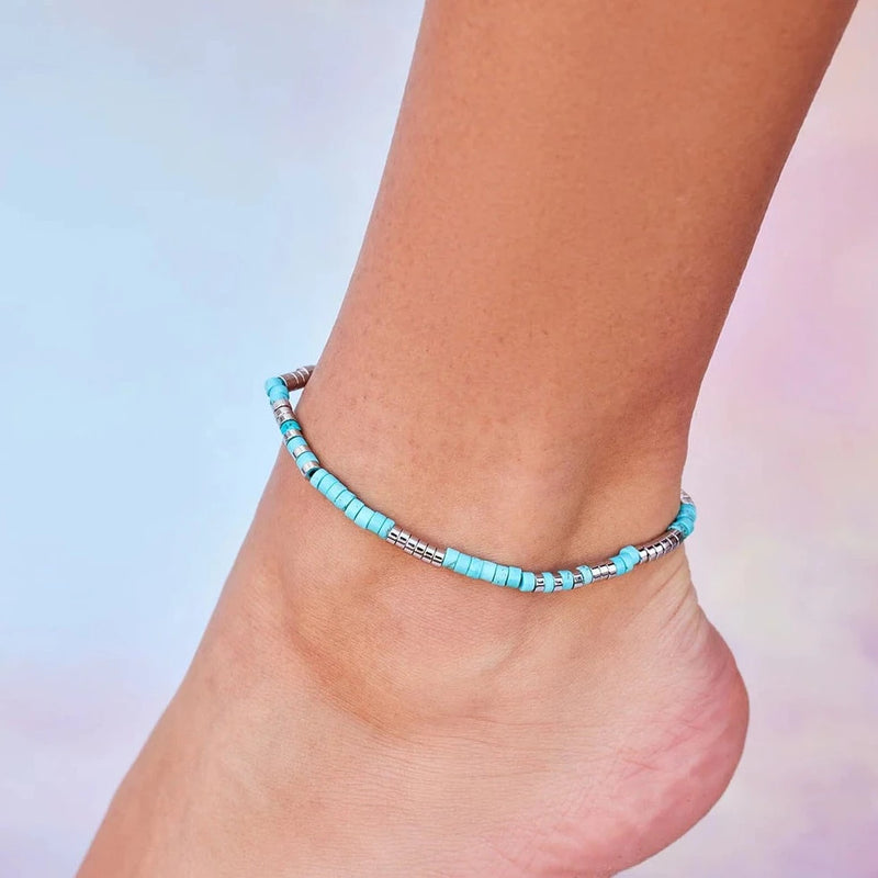Model is wearing anklet. Anklet has flat blue and silver beads all around it.