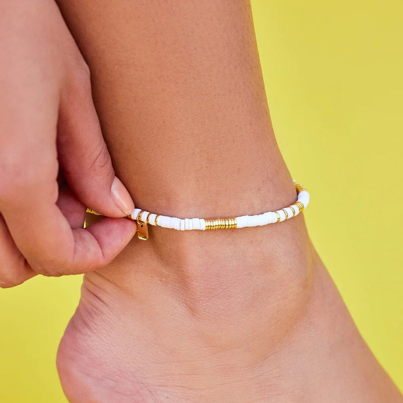 Close up of anklet on ankle with flat gold and white beads.