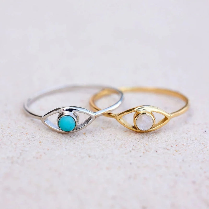 Shows both the silver and gold colorways of the ring on a flat surface. Both have eye with center stone.