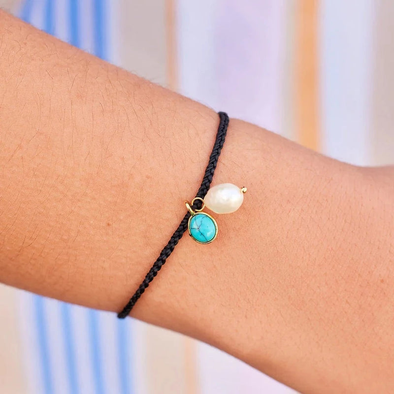 Shows model wearing the wax coated, mini braided bracelet on her wrist.  Bracelet features a fresh water pearl and turquoise stone charm.