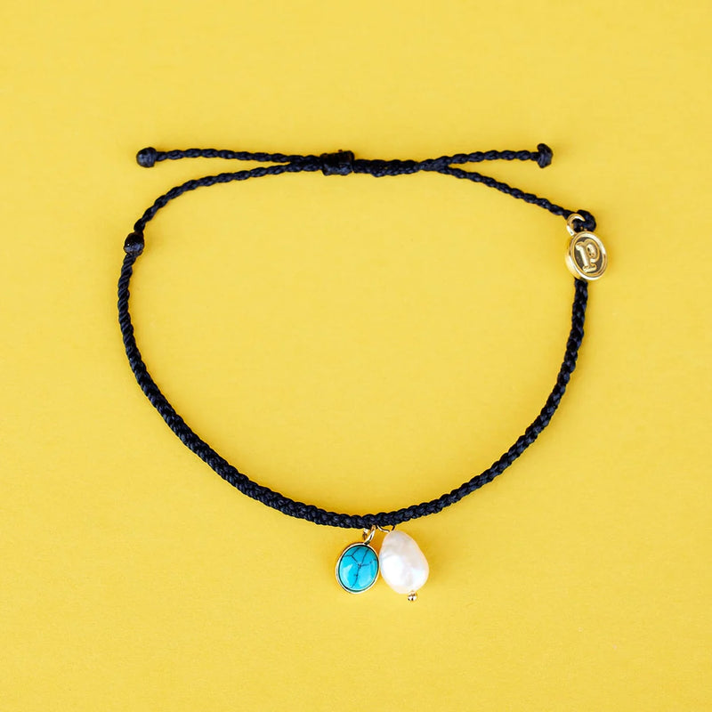 Shows the wax coated, mini braided bracelet laying on a flat surface. Bracelet features a fresh water pearl and turquoise stone charm. The adjustable length strings are visible. Also has a small circle charm with "P" in  center.