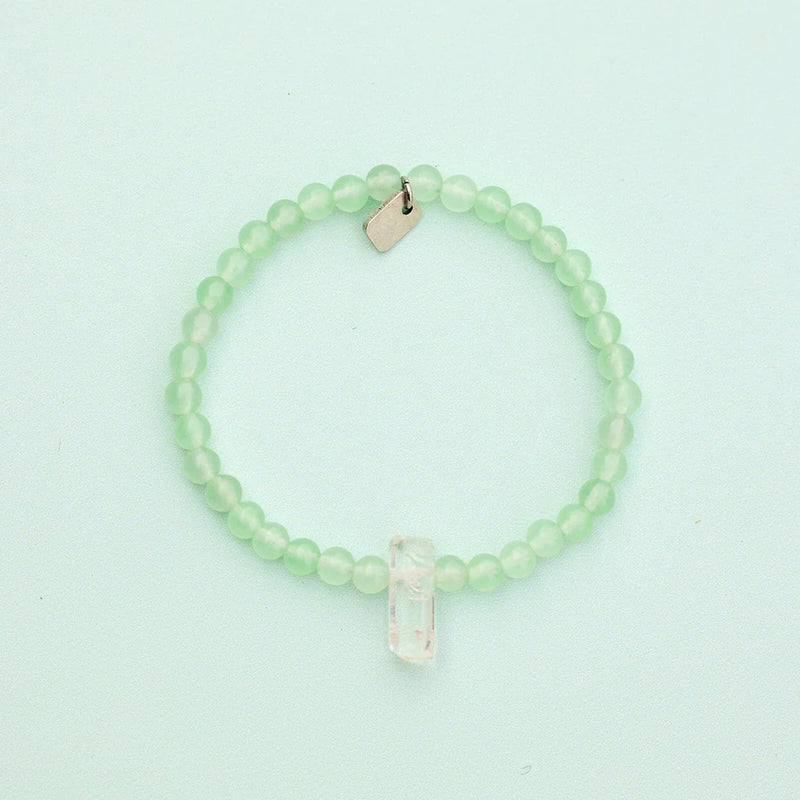 Shows bracelet on a flat surface. Green quartz beads with raw clear quartz center crystal.