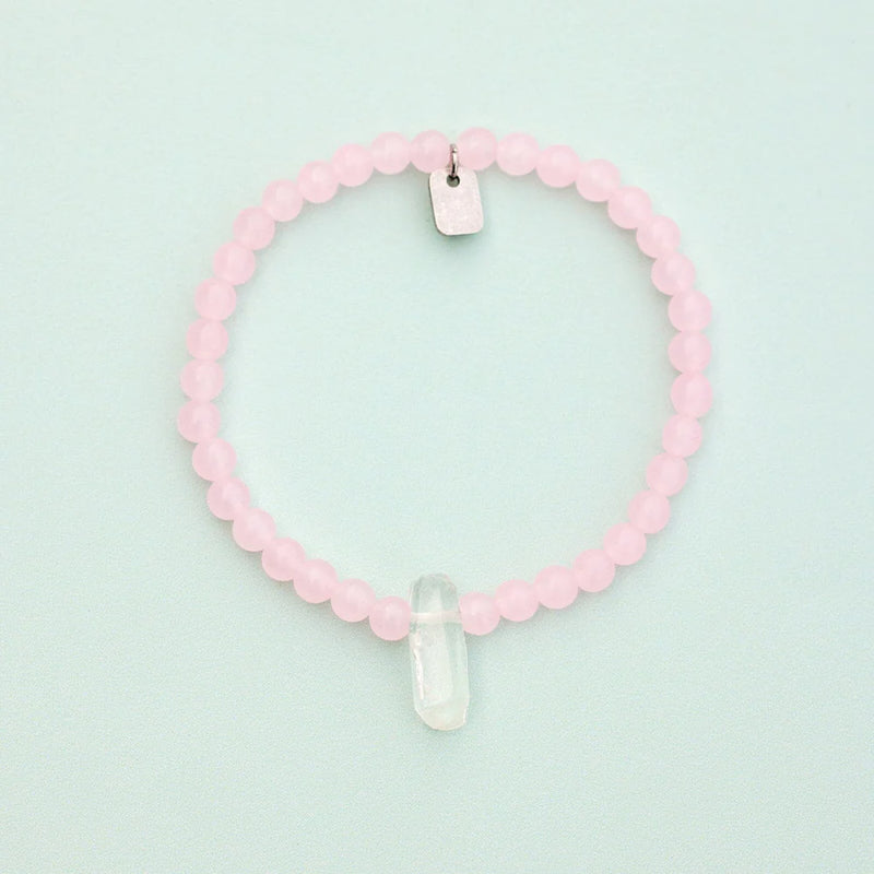 Shows bracelet on a flat surface. Rose quartz beads with raw clear quartz center crystal.