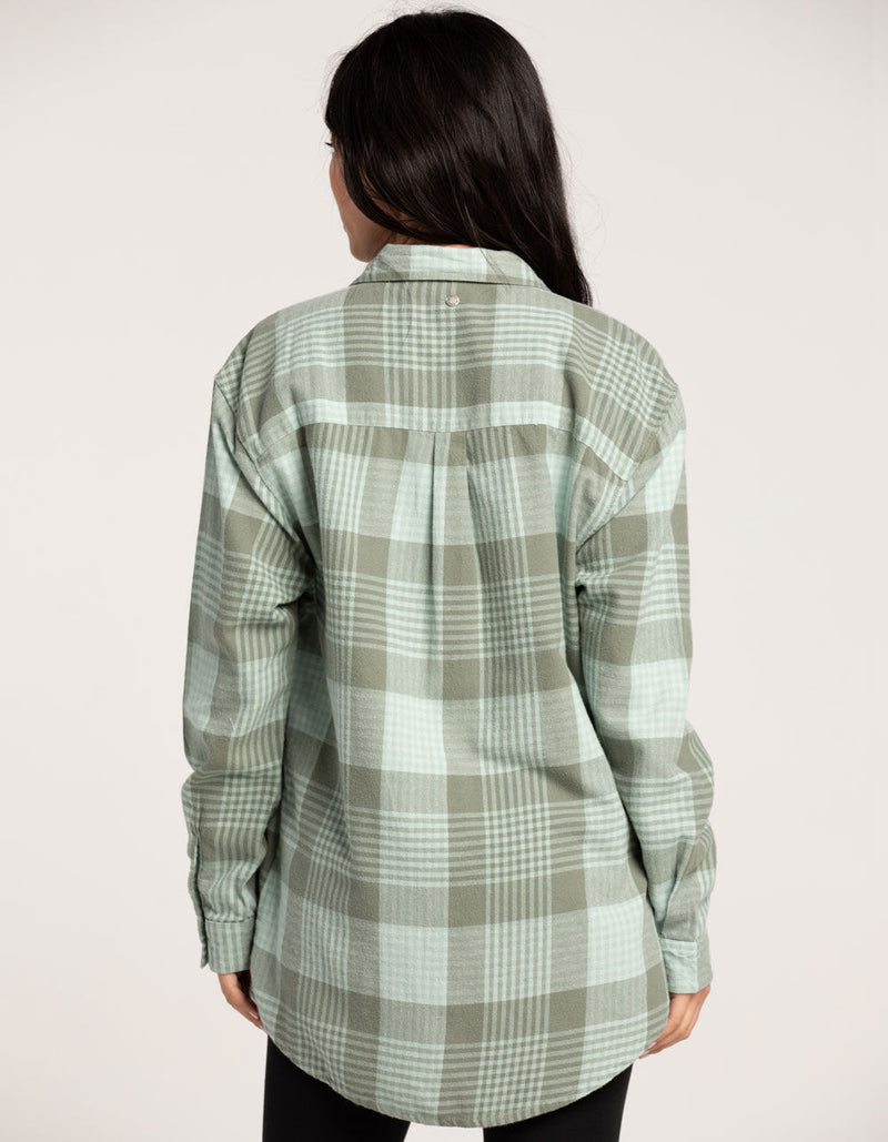 back view of model in shirt. shows the curved hemline and oversized fit. the dropped shoulders are visible as well as a horizontal seam across the back and some pleating.