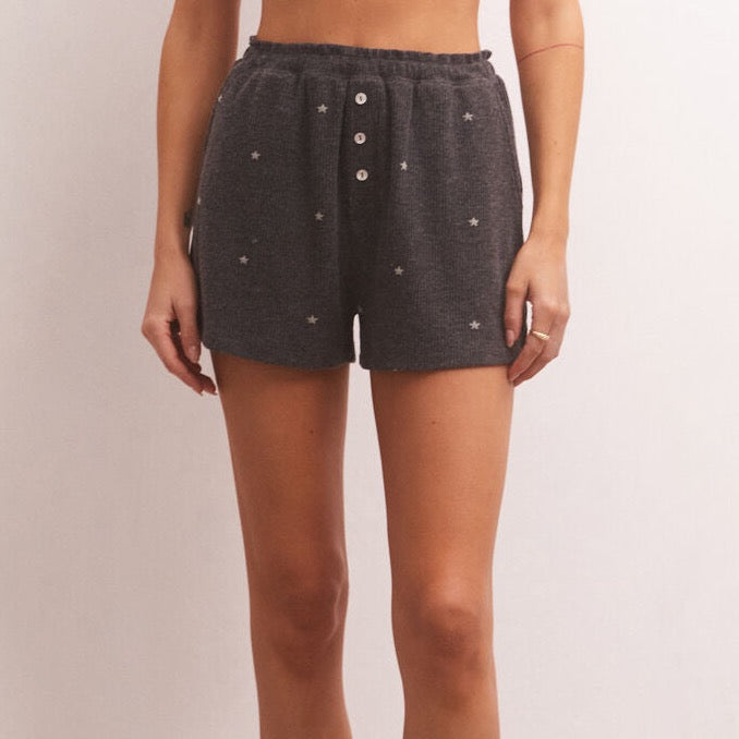 front view of model in shorts. shows the elastic waist with merrow edge and faux buttons in the front. mini star print all over.