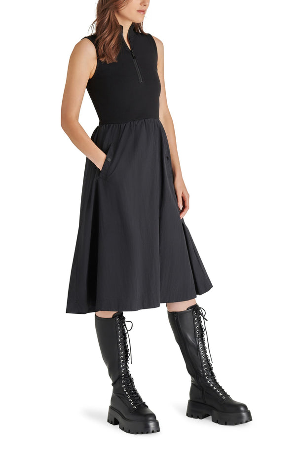 angled side view of model in dress. shows the knit bodice with fixed collar, half zip, midi length and lightweight skirt with pockets.