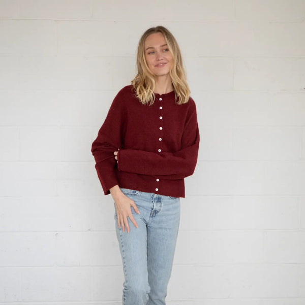 front view of the model wearing a wine color cardigan with blue jeans on a white background.