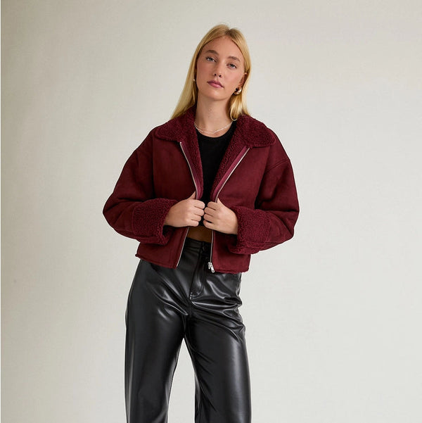 Person wearing a burgundy jacket and black pants on a plain background