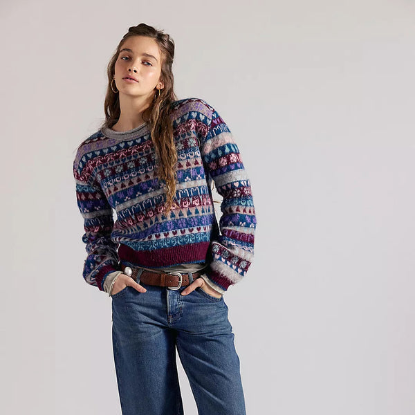 Person wearing a patterned sweater, jeans, and boots on a plain background