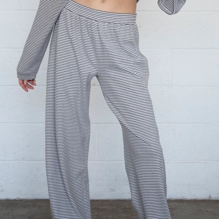 Person wearing striped pants and a long-sleeve top against a white brick wall.