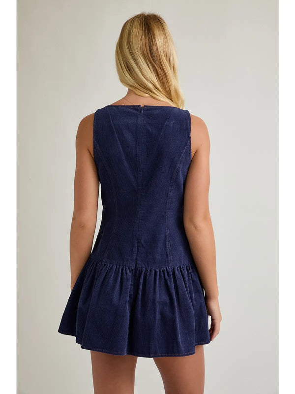 model wearing a navy dress against a cream background that is sleeveless. 