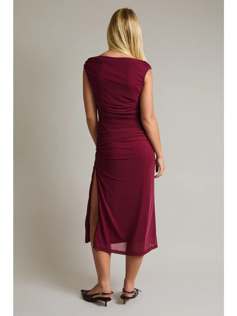 Woman wearing a burgundy dress with a slit on a plain background