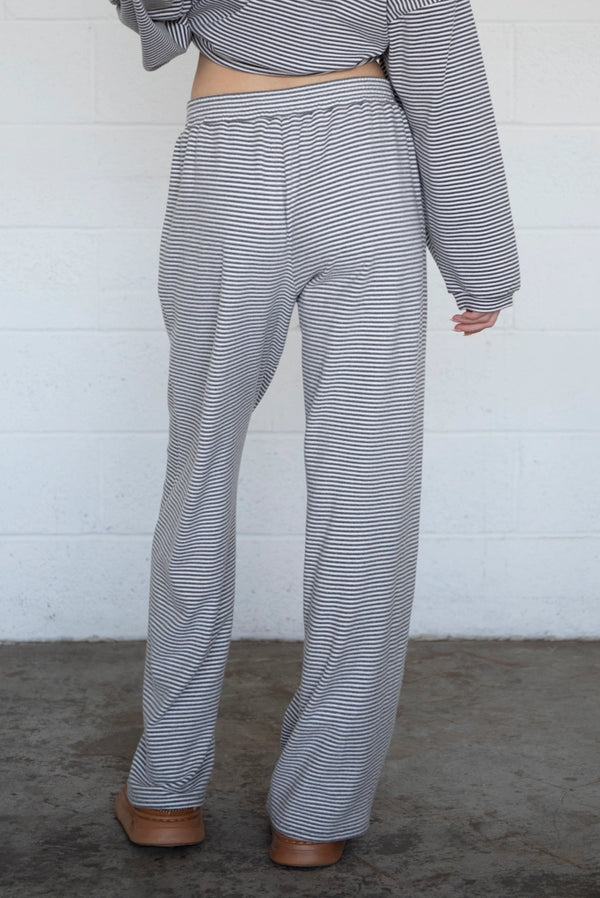 Person wearing a gray and white striped outfit with wide-leg pants against a white wall.