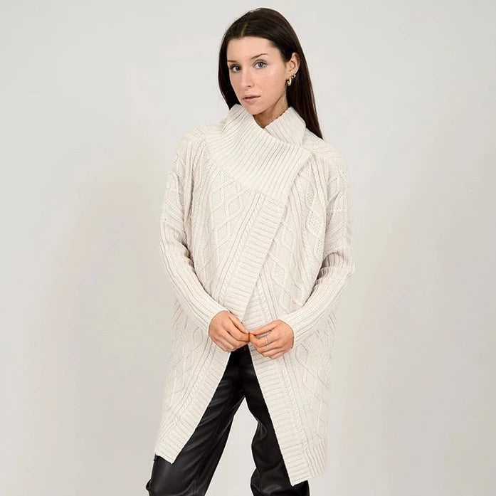 front view of model in cardigan. shows an oversized fit, cable knit fabrication and a cross over collar.
