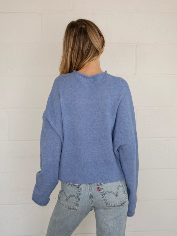 Woman wearing a blue cardigan and jeans against a white brick wall.