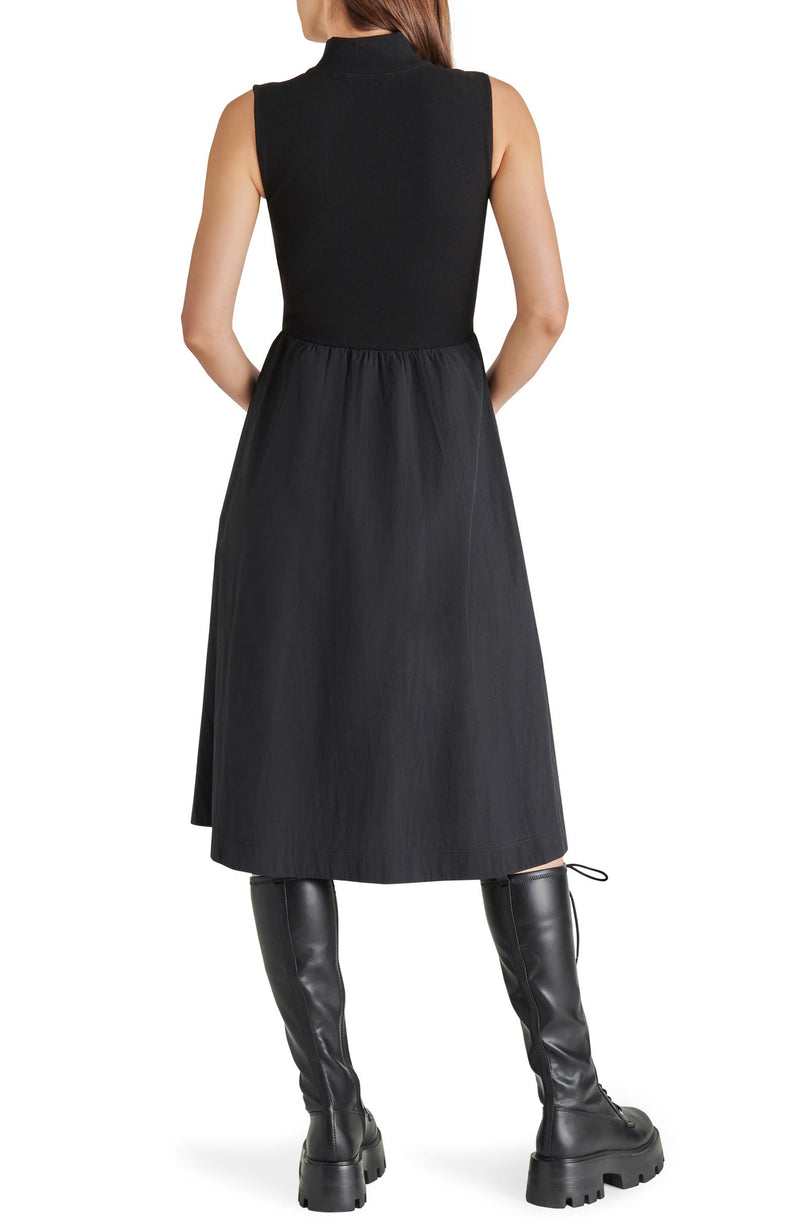 back view of model in dress. shows the knit bodice with high neck, sleeveless, lightweight midi skirt.